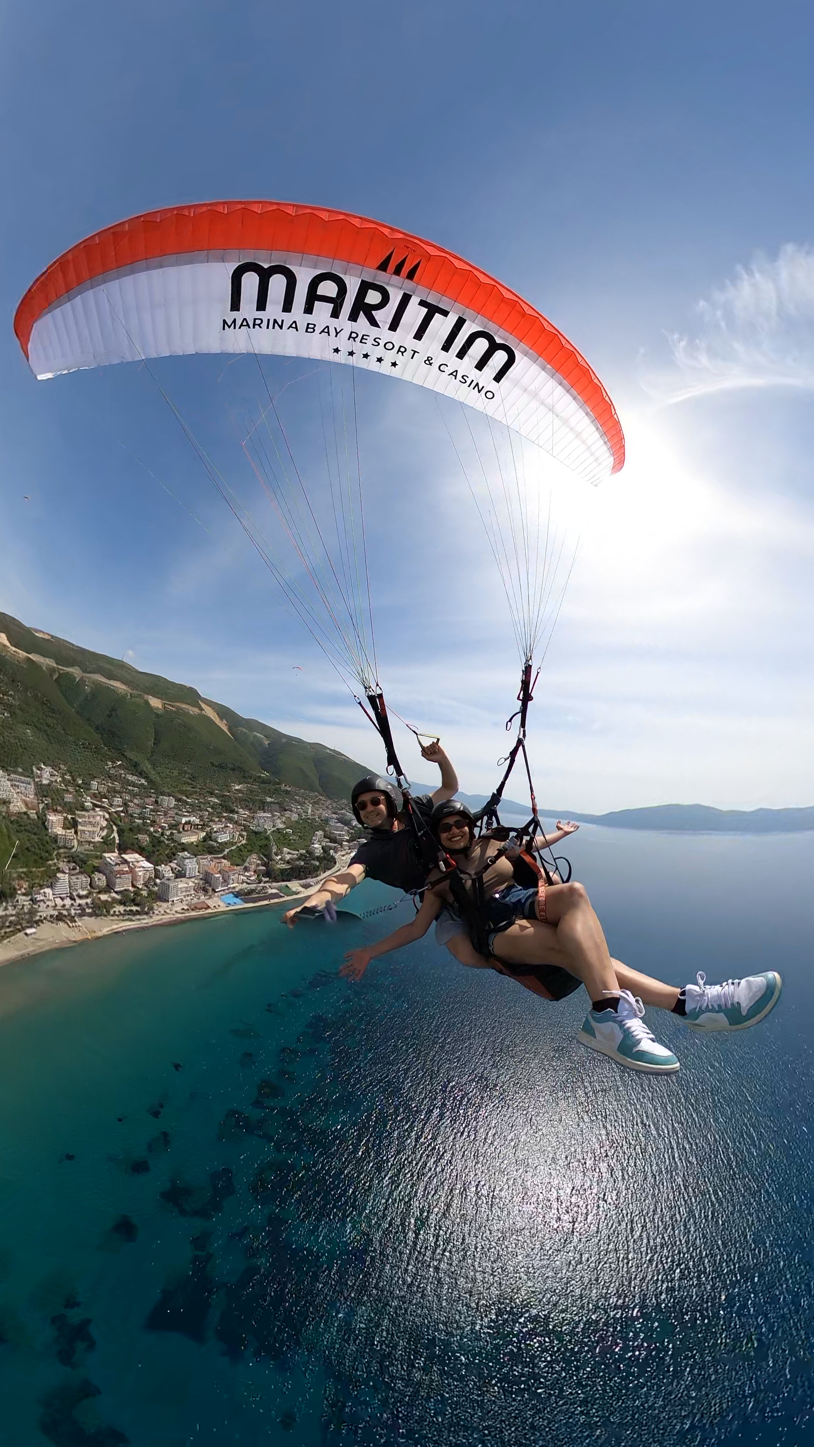 Tandem flight over turquoise Ionian Sea with paraglider wing visible