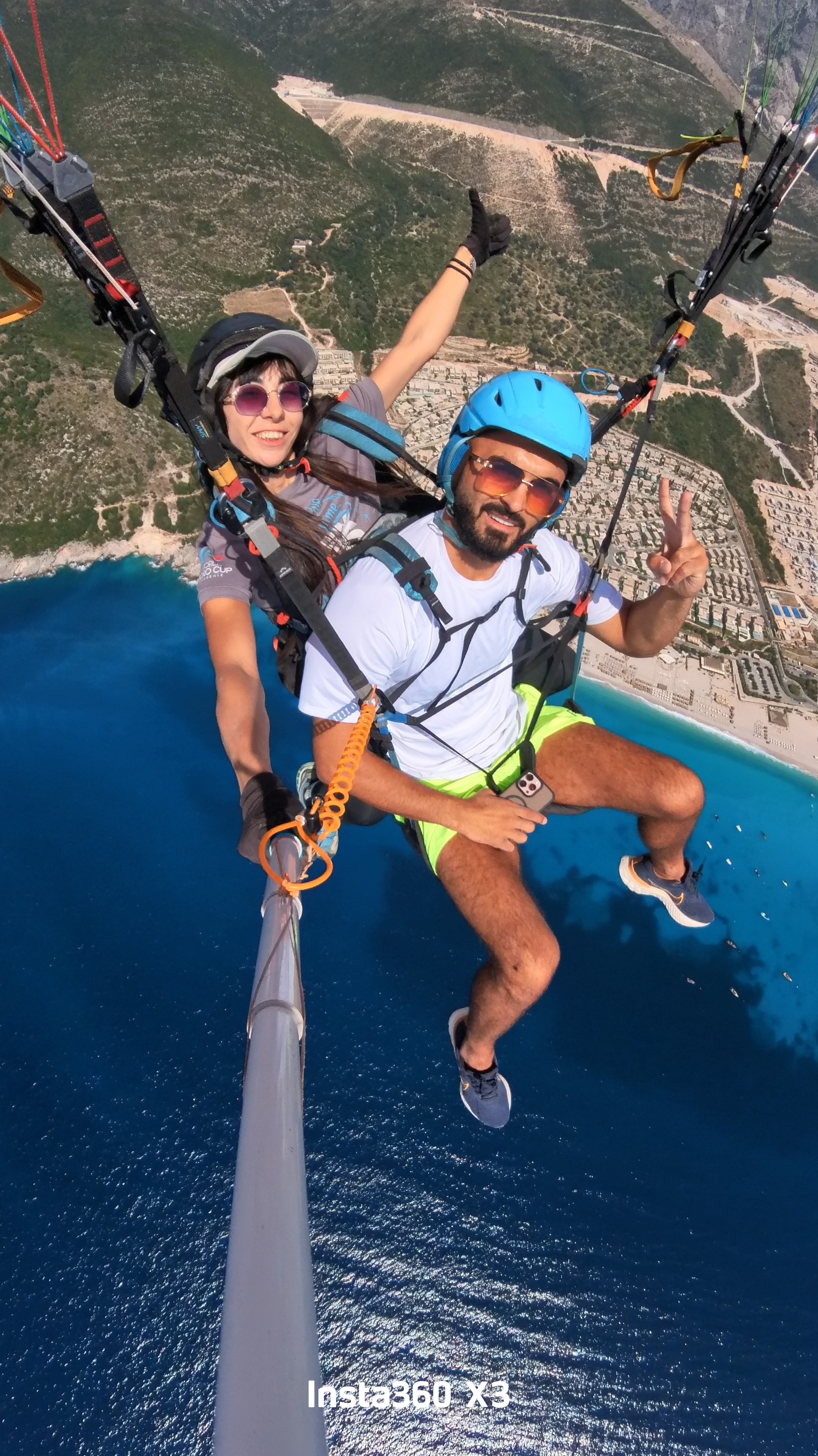 Tandem pair gliding over bright blue sea with the beach and coast below