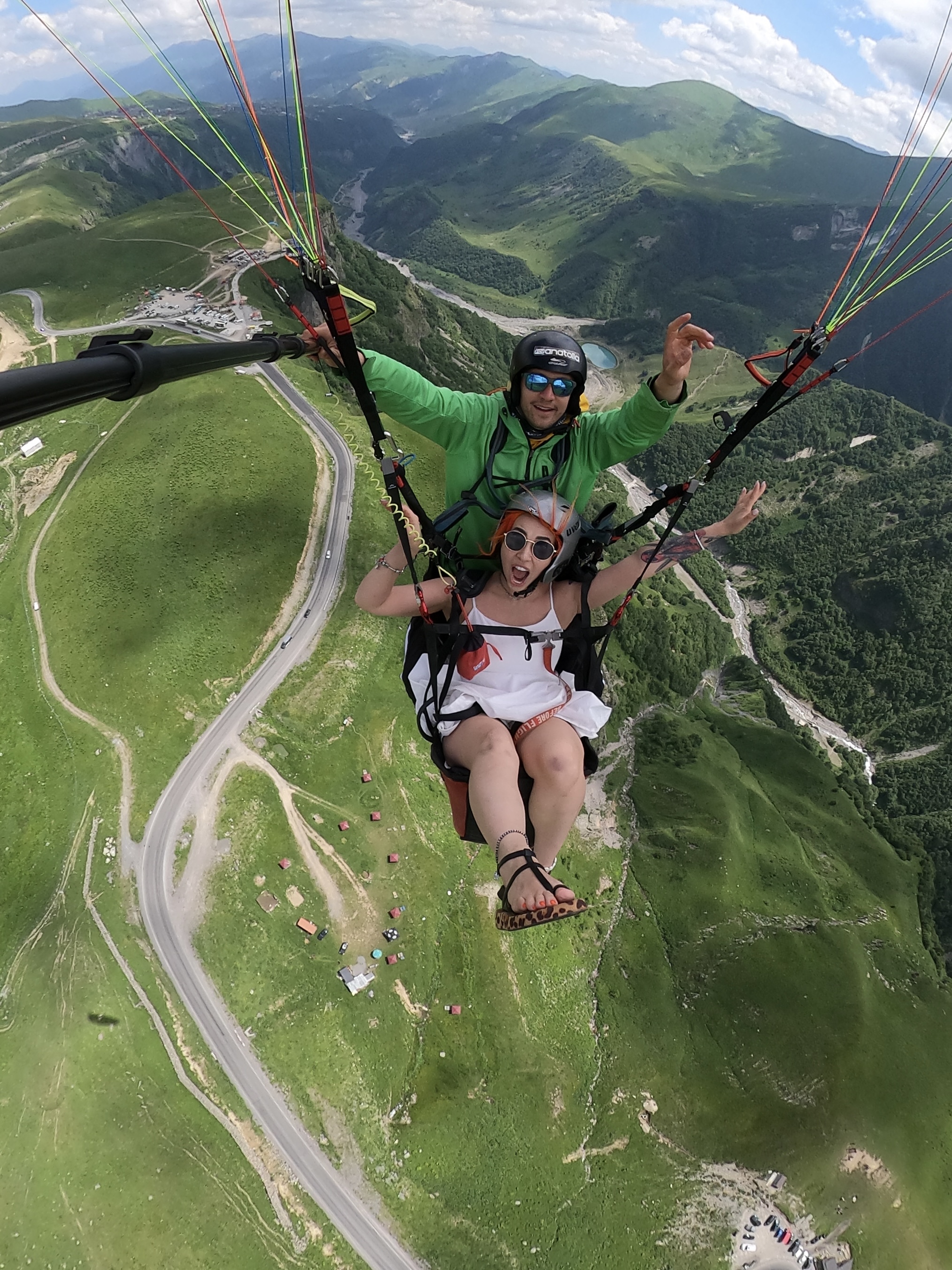 Tandem pilot and passenger flying above green mountain ridges near Vlora