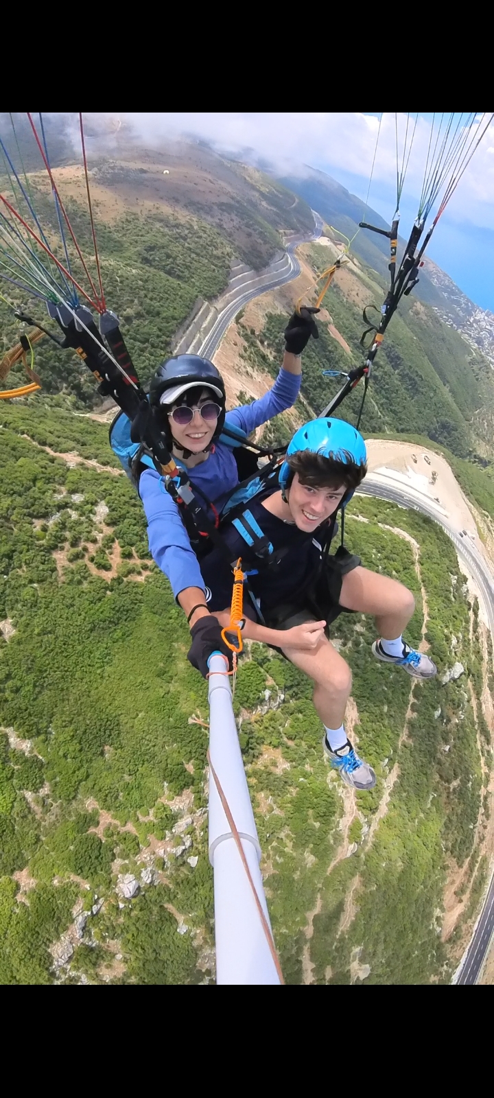 Tandem paragliding above coastal hills with sea visible in the distance